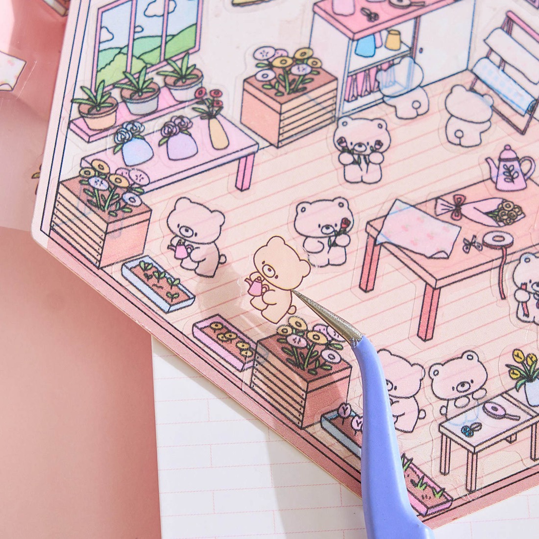 Tweezers placing a tiny bear sticker into the flower shop scene